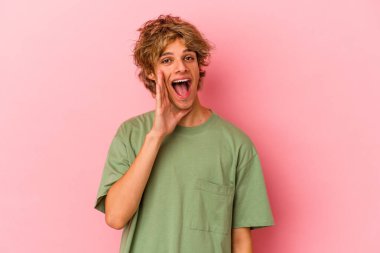 Makyajlı beyaz bir adam pembe arka planda izole edilmiş bağırıyor, gözleri açık ve elleri gergin tutuyor..