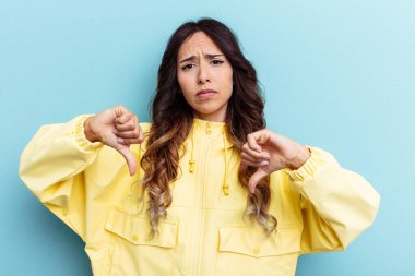 Mavi arka planda izole edilmiş genç Meksikalı kadın baş parmağını aşağı gösteriyor, hayal kırıklığı konsepti.