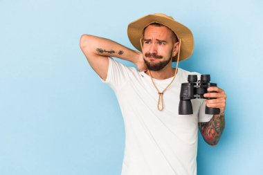 Mavi arka planda dürbün tutan, kafasının arkasına dokunan, düşünen ve bir seçim yapan beyaz dövmeli genç bir adam..