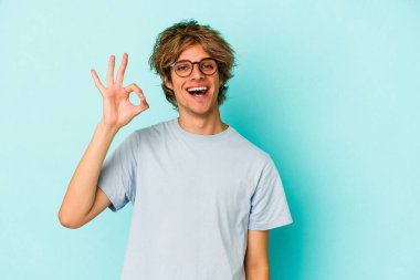 Makyajlı genç beyaz adam mavi arka planda izole edilmiş neşeli ve kendinden emin..