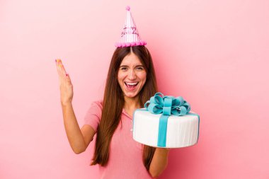 Pembe arka planda izole edilmiş bir doğum gününü kutlayan beyaz bir kadın hoş bir sürpriz alıyor, heyecanlı ve el kaldırıyor..