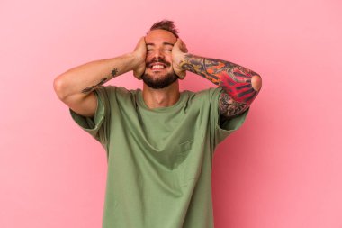 Pembe arka planda izole edilmiş dövmeleri olan beyaz bir genç ellerini başının üstünde tutarak gülüyor. Mutluluk kavramı.