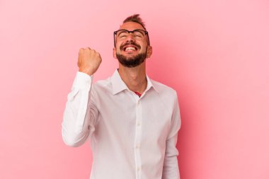 Pembe arka planda izole edilmiş dövmeleri olan beyaz bir adam zaferi, tutkuyu ve coşkuyu kutluyor..