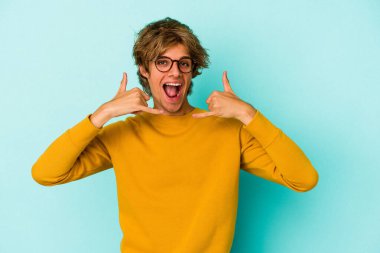 Mavi arka planda izole edilmiş beyaz makyajlı genç bir adam parmakları olan bir cep telefonu hareketi gösteriyor..