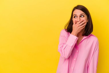 Genç beyaz kadın, sarı arka planda izole edilmiş. Düşünceli bir şekilde, ağzı elle kapatılmış bir fotokopi odasına bakıyor..