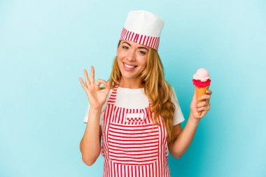 Kafkasyalı dondurma üreticisi kadın elinde dondurmayla mavi arka planda izole edilmiş neşeli ve kendinden emin bir şekilde iyi niyet gösteriyor..