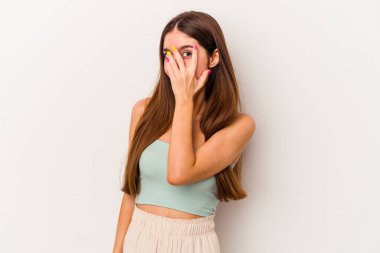 Beyaz arka planda izole edilmiş genç beyaz kadın kameraya parmaklarıyla göz kırpıyor, yüzünü kapatmaktan utanıyor..