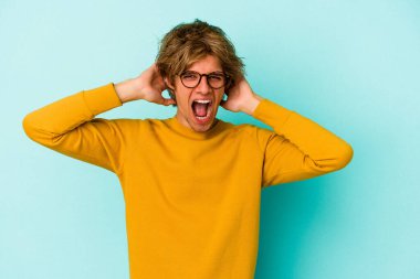 Makyajlı genç beyaz adam mavi arka planda izole edilmiş bağırıyor, çok heyecanlı, tutkulu, bir şeyden memnun..