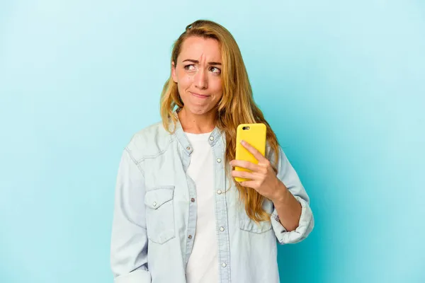 파란색 배경에서 휴대폰을 여성은 의심스럽고 불확실하다 — 스톡 사진