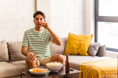 Genç melez adam kanepede oturmuş patlamış mısır yiyor parmakları dudaklarında bir sır saklıyor..