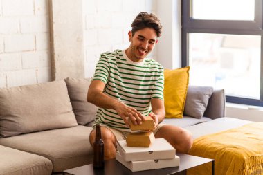 Genç melez adam pizza yiyor, burger yiyor ve bira içiyor.