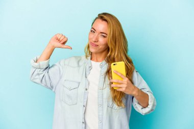 Mavi arka planda cep telefonu tutan beyaz kadın gururlu ve kendinden emin, örnek olarak.