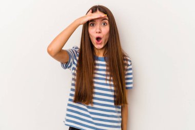 Beyaz arka planda soyutlanmış genç beyaz bir kadın çok uzaklara bakıyor ve elini alnına koyuyor..