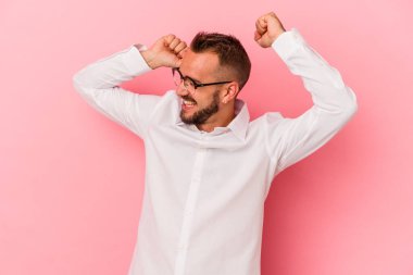 Pembe arka planda özel bir günü kutlayan dövmeleri olan beyaz bir genç adam atlıyor ve enerjisiyle kollarını kaldırıyor..