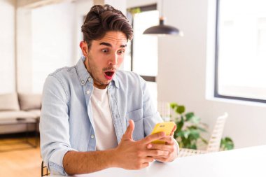 Genç melez adam mutfakta telefonla konuşuyor.