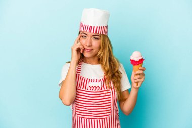 Kafkasyalı dondurma üreticisi kadın elinde dondurmayla mavi arka planda izole bir şekilde tapınağı işaret ediyor, düşünüyor, bir göreve odaklanıyor..