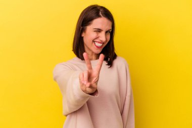 Sarı arka planda izole edilmiş genç beyaz kadın iki numarayı parmaklarıyla gösteriyor..