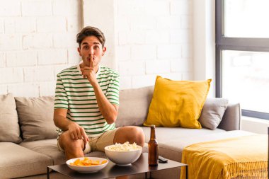 Genç melez adam kanepede oturmuş patlamış mısır yiyor ya sır saklıyor ya da sessizlik istiyor..