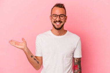 Pembe arka planda dövmeleri olan genç beyaz bir adam bir avuç içinde fotokopi alanı ve belinde bir el daha olduğunu gösteriyor..