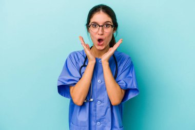 Kafkasyalı genç hemşire mavi arka planda izole edildi. Şaşırdı ve şok oldu..