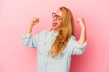 Pembe arka planda izole edilmiş beyaz sarışın kadın zafer kazandıktan sonra yumruğunu kaldırdı, kazanan konsept..