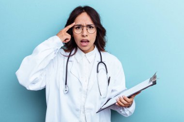 Mavi arka planda izole edilmiş genç bir Meksikalı kadın işaret parmağıyla hayal kırıklığı jesti gösteriyor..