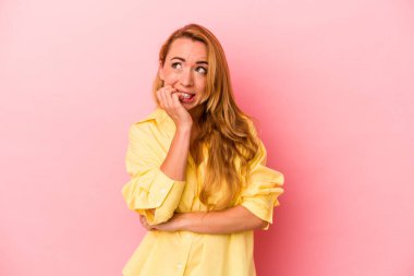 Pembe arka planda izole edilmiş, tırnak yiyen, gergin ve endişeli beyaz bir kadın..