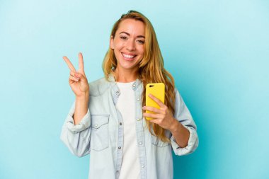 Mavi arka planda cep telefonu tutan beyaz kadın iki numarayı parmaklarıyla gösteriyor..