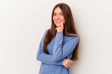 Beyaz arka planda izole edilmiş genç beyaz kadın mutlu ve kendinden emin gülümsüyor, elleriyle çenesine dokunuyor..