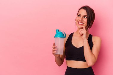 Pembe arka planda izole edilmiş protein içeceği içen beyaz bir kadın bir şeyin fotokopi odasına baktığını düşünüyor..