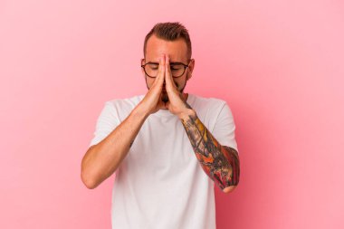 Pembe arka planda izole edilmiş dövmeleri olan beyaz bir genç. Ağız kenarında el ele dua ediyor. Kendinden emin..