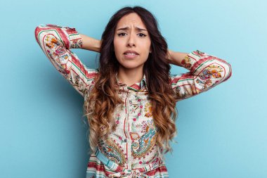 Mavi arka planda izole edilmiş genç Meksikalı kadın kafasının arkasına dokunuyor, düşünüyor ve bir seçim yapıyor..