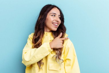 Mavi arka planda izole edilmiş genç Meksikalı kadın gülümseyen, neşeli ve keyifli bir kenara bakıyor..