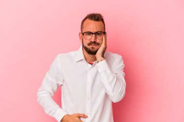 Pembe arka planda izole edilmiş dövmeleri olan beyaz genç adam yanaklarına sakso çekiyor ve yorgun bir ifade takınıyor. Yüz ifadesi kavramı.