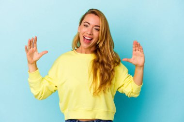 Beyaz kadın mavi arka planda izole edilmiş. Elinde avuç içi bir şeyle kameraya sunuyor..