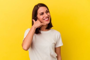 Sarı arka planda izole edilmiş genç beyaz kadın parmaklarıyla bir cep telefonu hareketi gösteriyor..