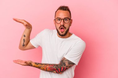 Pembe arka planda izole edilmiş beyaz dövmeli genç bir adam elleri arasında bir fotokopi alanı tutuyor..