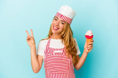 Kafkas dondurma üreticisi kadın elinde dondurmayla mavi arka planda izole edilmiş neşeli ve kaygısız parmaklarıyla barış sembolü gösteriyor..