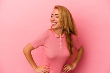 Beyaz tenli sarışın kadın pembe arka planda izole edilmiş. Kendine güvenen, ellerini kalçasında tutan..