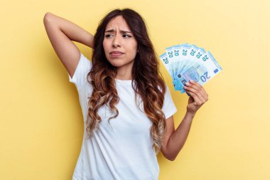 Sarı arka planda izole edilmiş banknotlar tutan genç melez kadın kafasının arkasına dokunuyor, düşünüyor ve bir seçim yapıyor..