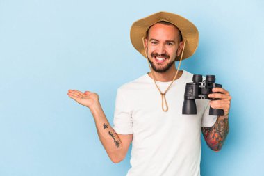 Mavi arka planda dürbün tutan beyaz dövmeli genç bir adam avucunun içinde bir fotokopi alanı olduğunu ve belinde başka bir el tuttuğunu gösteriyor..