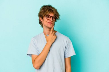 Makyajlı genç beyaz bir adam mavi arka planda izole edilmiş. Bir strateji planlıyor, bir iş yolu düşünüyor..