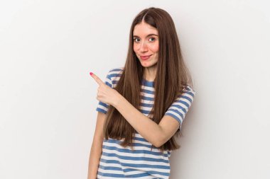 Beyaz arka planda izole edilmiş genç beyaz bir kadın gülümsüyor ve boş alanda bir şeyler gösteriyor..