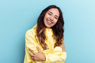 Mavi arka planda izole edilmiş genç Meksikalı kadın gülüyor ve eğleniyor..