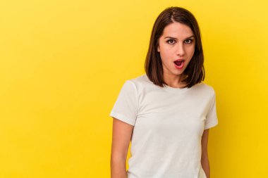 Sarı arka planda izole edilmiş genç beyaz kadın gördüğü bir şey yüzünden şoka uğruyor..