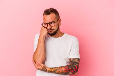 Pembe arka planda izole edilmiş dövmeleri olan, üzgün ve dalgın hisseden, kopyalama alanına bakan genç beyaz bir adam..