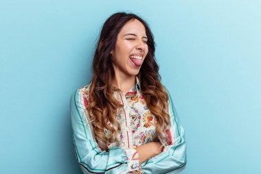 Mavi arka planda izole edilmiş genç Meksikalı kadın. Komik ve dost canlısı bir dil uzatıyor..