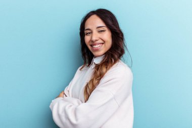 Mavi arka planda izole edilmiş genç Meksikalı kadın gülüyor ve eğleniyor..