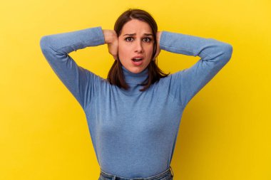 Sarı arka planda izole edilmiş genç, beyaz bir kadın. Kulakları kulaklarıyla kapatıyor. Çok fazla ses duymamaya çalışıyor..