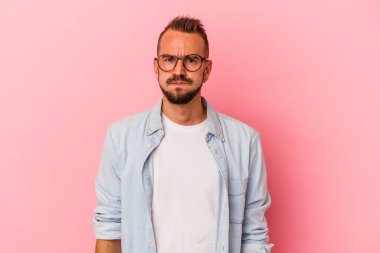 Pembe arka planda izole edilmiş dövmeleri olan beyaz genç adam yanaklarına sakso çekiyor ve yorgun bir ifade takınıyor. Yüz ifadesi kavramı.